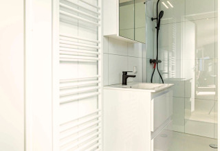 Moderne badkamer bij Silva Wellness met witte wastafel, grote spiegel, zwarte douche en handdoekradiator.