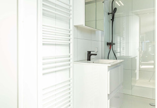 Baño moderno en Silva Wellness con tocador blanco, espejo grande, ducha negra y radiador para toallas.