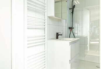 Baño moderno en Silva Wellness con tocador blanco, espejo grande, ducha negra y radiador para toallas.