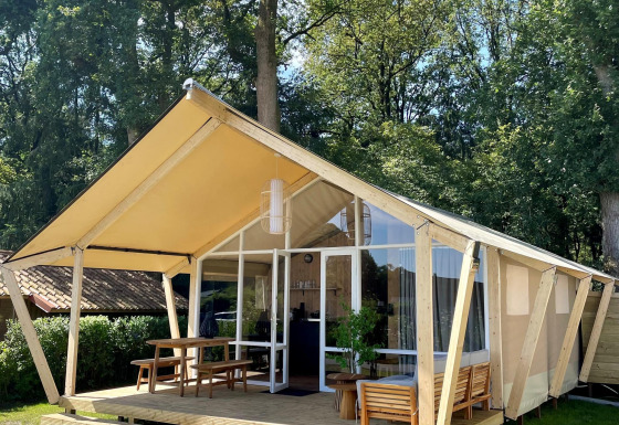 Safaritent Luna Lodge op Camping the Noetselerberg in Nederland met houten veranda en buitenzitje.
