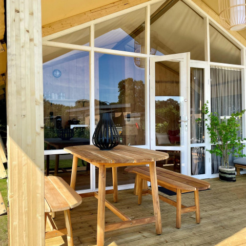 Outdoor wooden table and benches on the porch of a safari tent at Luna Lodge, Camping de Noetselerberg.