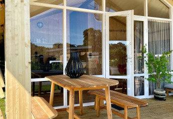 Houten tafel en banken op de veranda van een safaritent aan Luna Lodge, Camping de Noetselerberg, Nederland.