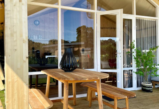 Outdoor wooden table and benches on the porch of a safari tent at Luna Lodge, Camping de Noetselerberg.