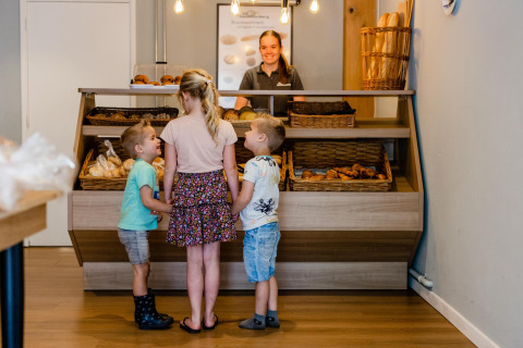 Tre bambini ordinano dolci al banco di panetteria del Luna Lodge, Camping Noetselerberg, Paesi Bassi.