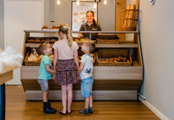 Tre bambini ordinano dolci al banco di panetteria del Luna Lodge, Camping Noetselerberg, Paesi Bassi.