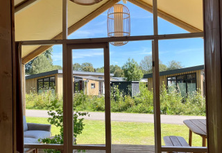 Uitzicht vanuit de Luna Lodge safaritent op Camping de Noetselerberg, met moderne chalets op de achtergrond.