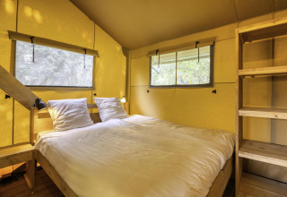 Interior de una tienda safari en Stardust 40 Family Lodge, Arden Parks, con cama doble y estantería de madera.