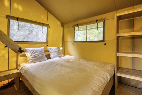 Interior of a safari tent at Stardust 40 Family Lodge, Arden Parks, featuring a double bed and wooden shelves.