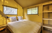 Interior of a safari tent at Stardust 40 Family Lodge, Arden Parks, featuring a double bed and wooden shelves.