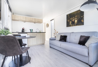 Interior luminoso de una casa flotante con cocina moderna, mesa de comedor y sofá en Harbour Lodge Amsterdam.