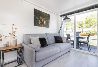Lichte leefruimte op woonboot Harbour Lodge Amsterdam met zetel, decoratie en uitzicht op water.