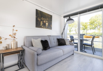 Lichte zithoek op woonboot Harbour Lodge Amsterdam met bank, decoratie en uitzicht op het water.
