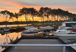 Woonboot bij Marina Parcs Amsterdam, omringd door boten en zonsondergang, gezien vanaf Harbour Lodge Amsterdam.