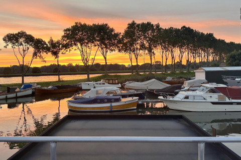 Woonboot bij Marina Parcs Amsterdam met meerdere boten en zonsondergang, gezien vanaf Harbour Lodge Amsterdam.
