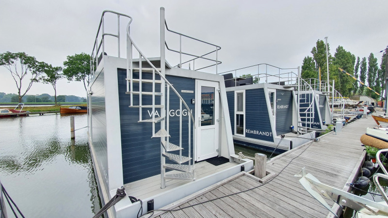 Modern houseboats with rooftop patios docked at Marina Parcs Amsterdam, Netherlands, alongside a wooden pier.