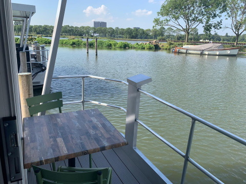 Vista desde la casa flotante Harbour Lodge Amsterdam en Marina Parcs con mesa y sillas junto al agua.