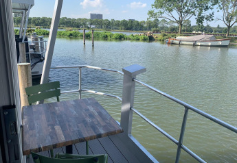 Vista desde la casa flotante Harbour Lodge Amsterdam en Marina Parcs con mesa y sillas junto al agua.