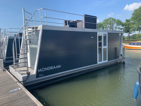 Woonboot genaamd Harbour Lodge Amsterdam aangemeerd bij Marina Parcs Amsterdam op een zonnige dag.