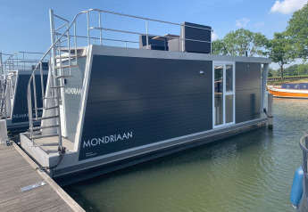 Hausboot namens Harbour Lodge Amsterdam im Wasser bei Marina Parcs Amsterdam, Niederlande, bei Sonnenschein.