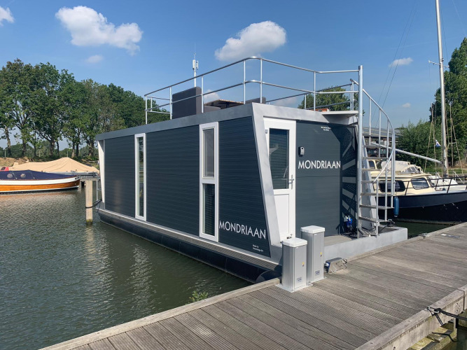 A modern houseboat named Mondriaan docked at Marina Parcs Amsterdam in the Netherlands on a sunny day.