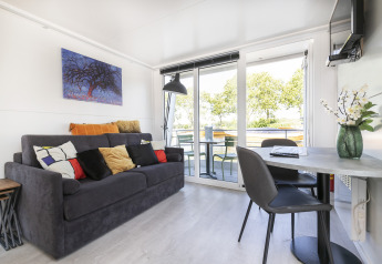 Stue på en husbåd, Harbour Lodge Amsterdam, med sofa, bord, stole og udsigt over vandet.