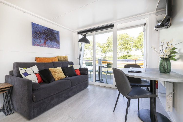 Living room of a houseboat, Harbour Lodge Amsterdam, with sofa, table, chairs and water view.