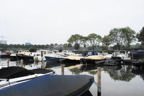 Casa flotante en Harbour Lodge Amsterdam, Marina Parcs, con varios barcos y árboles en el fondo.