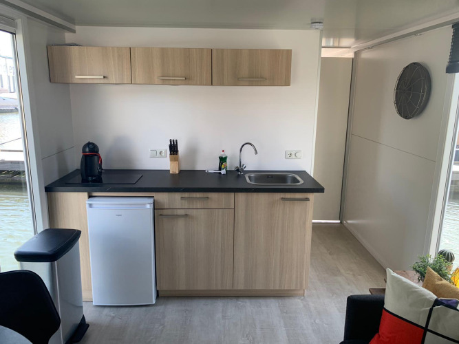 Modern houseboat kitchenette at Marina Parcs Amsterdam with wood cabinets, sink, stovetop and mini fridge.