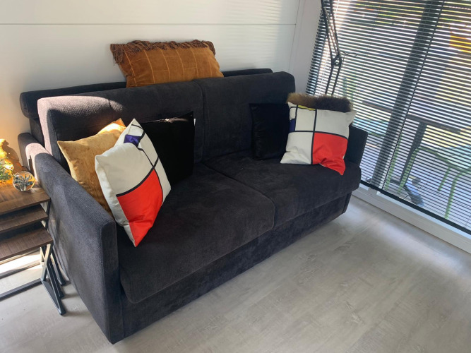 Modern living area on houseboat Harbour Lodge Amsterdam featuring comfy sofa, designer pillows, and windows.