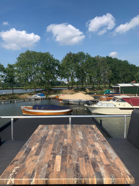 Zicht vanaf een woonboot bij Marina Parcs Amsterdam, met boten, bomen en blauwe lucht met wolken in Nederland.