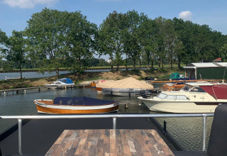 Zicht vanaf een woonboot bij Marina Parcs Amsterdam, met boten, bomen en blauwe lucht met wolken in Nederland.