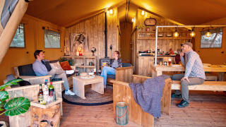 Quattro persone si rilassano in una tenda safari accogliente con mobili rustici a Marina Parcs Almere, Olanda.