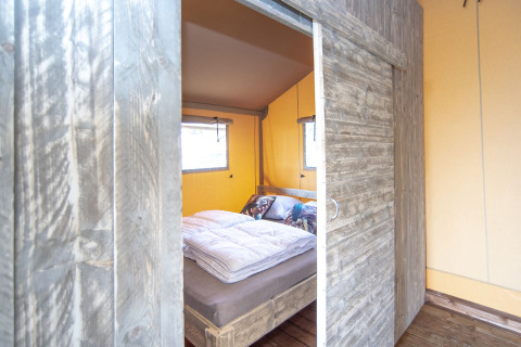 Entrada a un dormitorio con cama rústica de madera en una tienda Safari lodge XL en Marina Parcs Almere, Países Bajos.