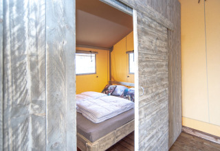 Entrada a un dormitorio con cama rústica de madera en una tienda Safari lodge XL en Marina Parcs Almere, Países Bajos.