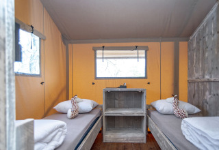 Intérieur de la tente Safari lodge XL à Marina Parcs Almere avec lits simples et peluches girafe décoratives.