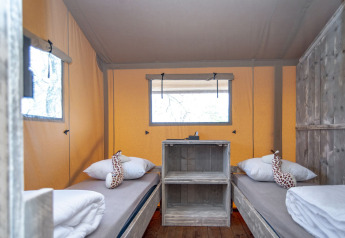 Intérieur de la tente Safari lodge XL à Marina Parcs Almere avec lits simples et peluches girafe décoratives.