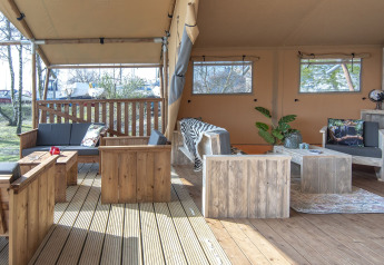 Grande tente safari lodge avec mobilier en bois et coin salon confortable à Marina Parcs Almere, Pays-Bas.