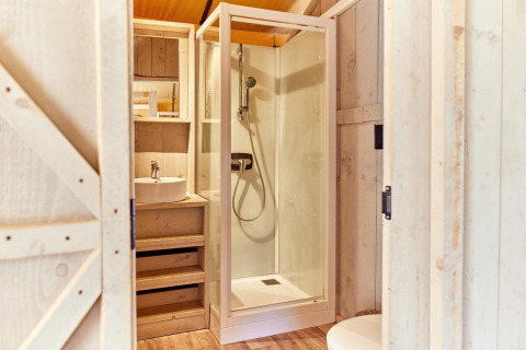 Baño con cabina de ducha, lavabo y decoración de madera en Villatent Outback, Camping Au Clos de La Chaume, Francia.