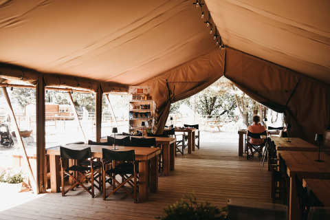 Innenansicht eines Gemeinschaftszeltes mit Holztischen und Stühlen auf Camping Luna del Monte in Umbrien, Italien.