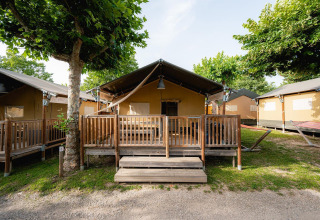 Tienda safari 'Villatent Outback' con porche de madera en Campeggio del Garda, Italia, rodeada de árboles.