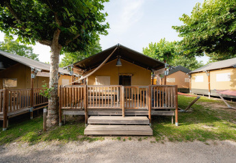 Safaritent 'Villatent Outback' met houten veranda op Campeggio del Garda in Italië, omringd door bomen.