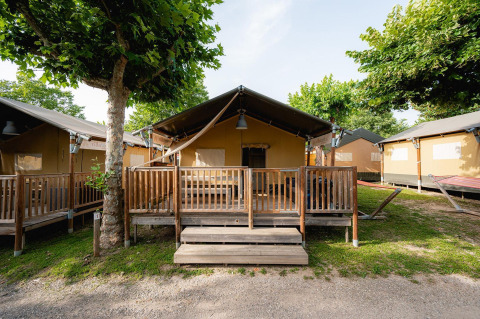 Tenda safari 'Villatent Outback' con veranda in legno al Campeggio del Garda in Italia, circondata da alberi.