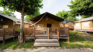 Safari telt 'Villatent Outback' med træveranda på Campeggio del Garda campingplads i Italien, omgivet af træer.