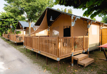 Tente safari Villatent Outback avec terrasse en bois au Campeggio del Garda, en Italie, entourée d’arbres verts.