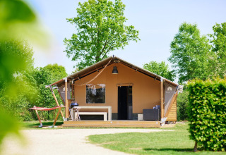 Tienda safari Villatent Nomad en Camping Betuwestrand, Países Bajos, rodeada de árboles y naturaleza verde.