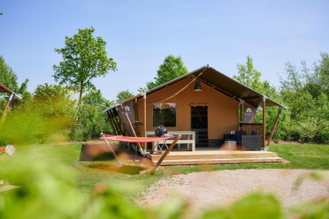 Tienda safari Villatent Nomad en Camping Betuwestrand, Países Bajos, rodeada de vegetación y árboles.