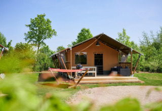 Tienda safari Villatent Nomad en Camping Betuwestrand, Países Bajos, rodeada de vegetación y árboles.