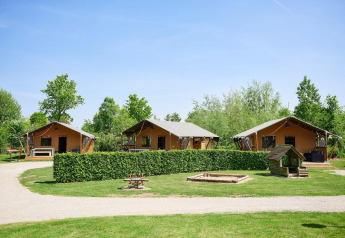 Tende safari Villatent Nomad al Camping Betuwestrand nei Paesi Bassi, immerse nel verde e sotto un cielo sereno.
