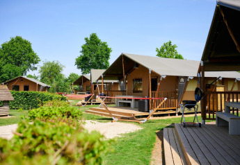 Tende safari al Camping Betuwestrand nei Paesi Bassi con pontili in legno e prati verdi soleggiati.