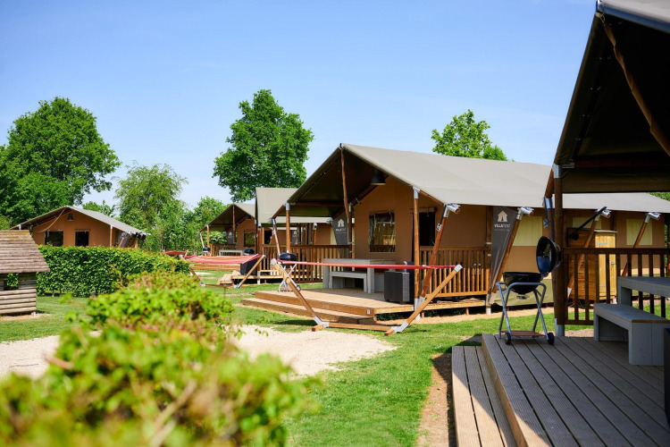 Safaritenten bij Camping Betuwestrand in Nederland met houten veranda’s, veel groen en zonnige lucht.